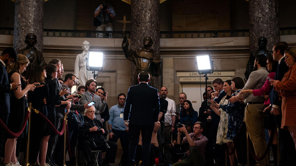 House Speaker Mike Johnson speaking to the press, in a wide image from behind